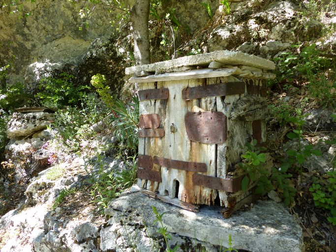 Ruche en planche, installée dans un petit rucher au pied sud d'un rocher. Quartier du Moulin.